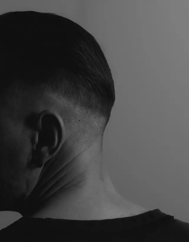 The back of a man&rsquo;s head and neck in black and white, with hair cut short and tapered close at the ear and nape.