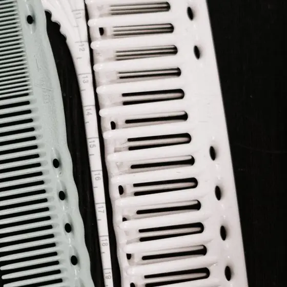 Two white and pale green cutting combs with wide and fine teeth, one with a ruler marked along its edge, on a black table.